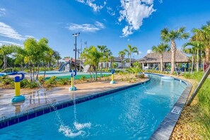 Una piscina con fuentes, palmeras y una estructura de techo de paja.