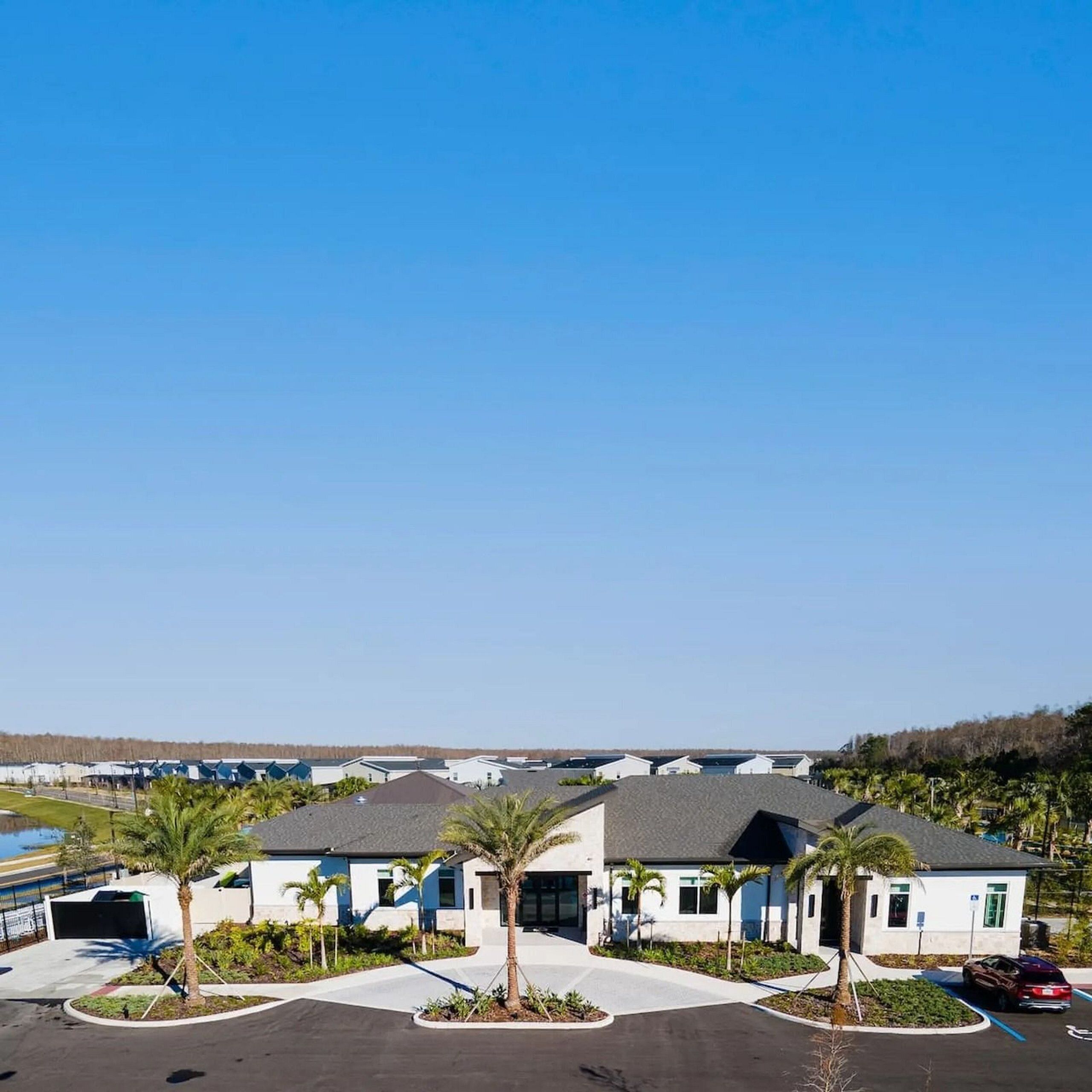Ein modernes Hotel mit Parkplatz, Palmen und blauem Himmel.