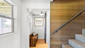 Un pasillo con un banco de madera, una escalera con barandilla metálica y un cartel enmarcado que dice "STAY awake".