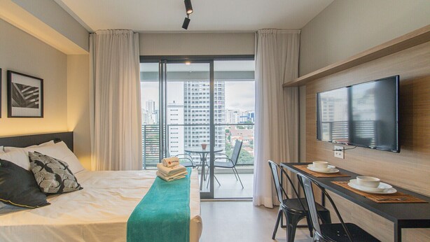 Habitación de hotel con cama, escritorio con silla, televisor y balcón con vista a la ciudad.