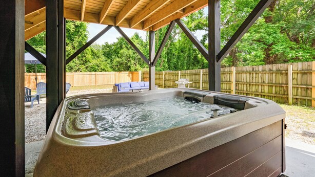 A hot tub under a wooden pergola with a wooden fence and trees in the background. - Boho 5BR Modern Villa•Hot Tub•Grill•Patio•Backyard (Raleigh)