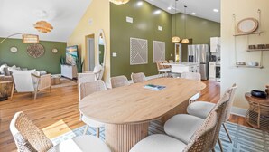 A modern kitchen with white cabinets, a stainless steel refrigerator, and a dining area with a wooden table and wicker chairs. - Boho 5BR Modern Villa•Hot Tub•Grill•Patio•Backyard (Raleigh)