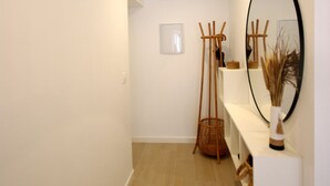 A hallway with a white wall, a wooden floor, a mirror, and a shelf with a vase. - 30 - Livingtarifa El Poniente (Tarifa)