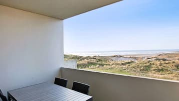A balcony with a table and chairs, overlooking a coastal landscape.