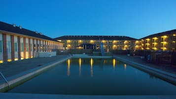 A swimming pool with a fountain in the center, surrounded by a building with multiple balconies and windows.