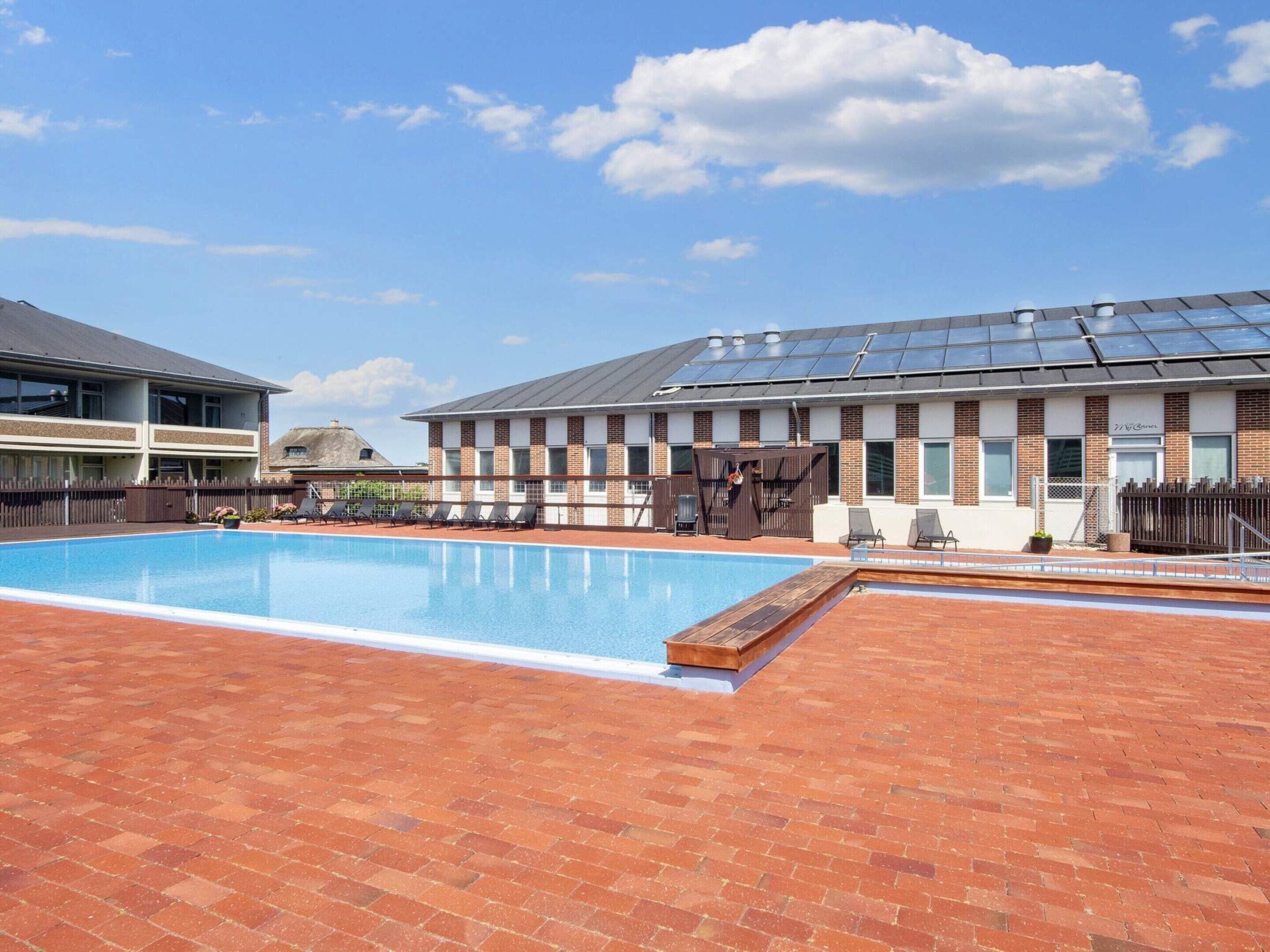 Une piscine avec des chaises longues et un bâtiment équipé de panneaux solaires.