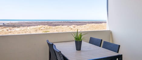 Un balcón con mesa y sillas, una planta en maceta y vista a la playa.