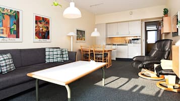 Un espacio habitable compacto con sofá, mesa de comedor, zona de cocina y una silla de cuero negro.