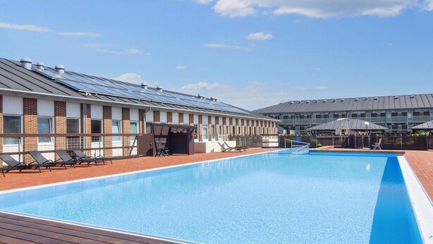 A swimming pool with sun loungers and a wooden deck, surrounded by buildings with solar panels. - 4 Person Holiday Park Home in Fano (Fano)