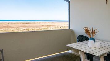 A balcony with a view of the beach, a table with a vase and a chair, and a wall with a small sign.