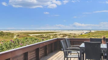 A deck with outdoor seating overlooking a beach and dunes.