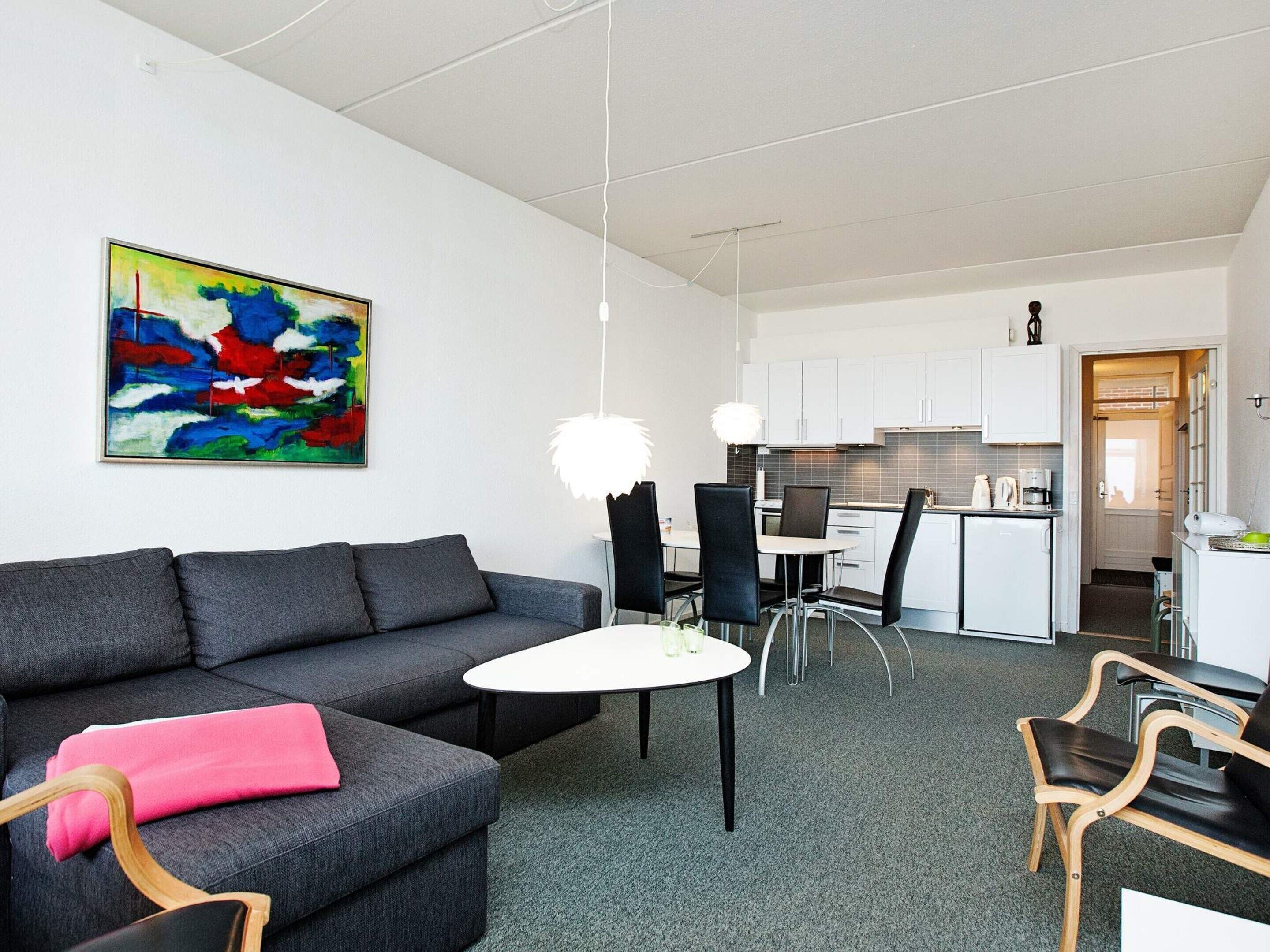A modern living room with a grey sofa, a small round table, and black chairs. A colorful abstract painting is on the wall.