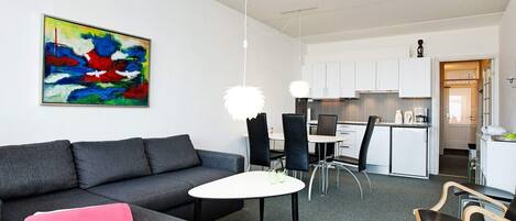 A modern living room with a grey sofa, a small round table, and black chairs. A colorful abstract painting is on the wall.