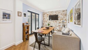 Een moderne woonkamer met een houten eettafel, een bank en een televisie bevestigd aan een bakstenen muur.
