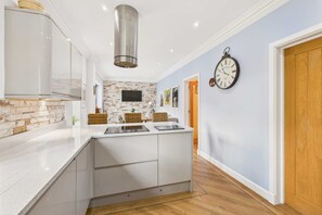 Une cuisine moderne avec un îlot central, des meubles blancs, un mur d’accent en briques et une horloge au mur.