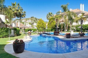 A swimming pool with a curved edge, surrounded by palm trees and lounge chairs. - Aloha Hills Club apartment in Marbella with pool (Marbella)