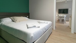 Ein ordentlich gemachtes Bett mit weißen Leinen und einem gefalteten Handtuch daneben.