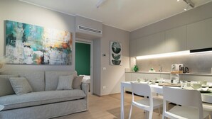 Ein modernes Wohnzimmer mit einem grauen Sofa, weißen Stühlen und einem Esstisch für vier Personen.