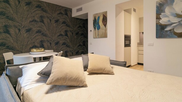 A bedroom with a bed, two pillows, a nightstand, a small table with a lamp, and a wall with a leaf pattern.