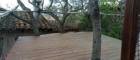 Una terraza de madera con una barandilla de cuerda y árboles al fondo.
