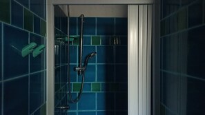 A shower with a handheld showerhead and a wall-mounted faucet, set against a tiled wall with a blue and green pattern. - Domos De Badas - Trilocale (Porto Ottiolu)