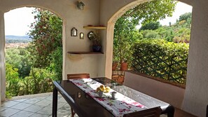 A patio with a table set for two, surrounded by greenery and a scenic view. - Domos De Badas - Trilocale (Porto Ottiolu)