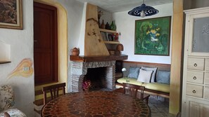A cozy dining area with a stone-tiled table, a wooden bench, and a fireplace with a rustic mantle. - Domos De Badas - Trilocale (Porto Ottiolu)