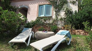 A patio with two sun loungers, a stone wall, and a window with blue shutters. - Domos De Badas - Trilocale (Porto Ottiolu)