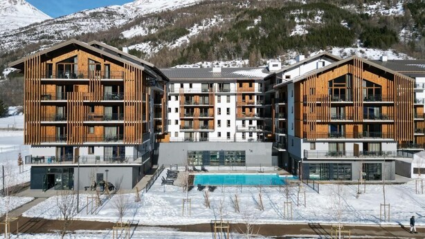 A modern building with multiple balconies, a swimming pool, and a snowy mountain backdrop. - Wifi, swimming pool, sauna, hammam, balcony, tv, ski locker, 44-53m², Serre Chevalier (La Salle-les-Alpes)