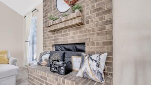 Una sala de estar con chimenea de ladrillo, un sofá blanco y almohadones decorativos.