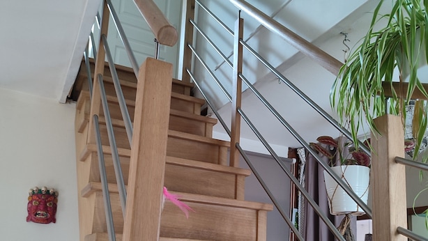 A wooden staircase with metal railings, a potted plant, and a decorative mask on the wall. - Chambre en Brière with jacuzzi near Guérande (Saint-Lyphard)