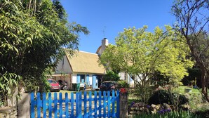 A rural house with a thatched roof, surrounded by a blue fence, and a garden with various plants and flowers. - Chambre en Brière with jacuzzi near Guérande (Saint-Lyphard)