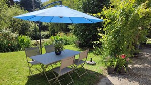 An outdoor patio with a table and chairs, a blue umbrella, and potted plants. - Chambre en Brière with jacuzzi near Guérande (Saint-Lyphard)