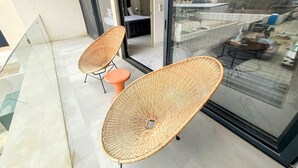 A balcony with wicker chairs and a glass door leading to a bedroom.