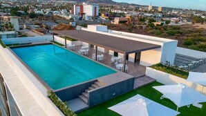 A rooftop pool with a view of the city, outdoor seating, and a covered area.