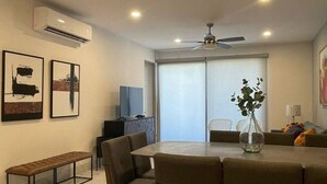 A modern dining area with a round table, chairs, and a bench. There is a ceiling fan, recessed lighting, and an air conditioning unit.