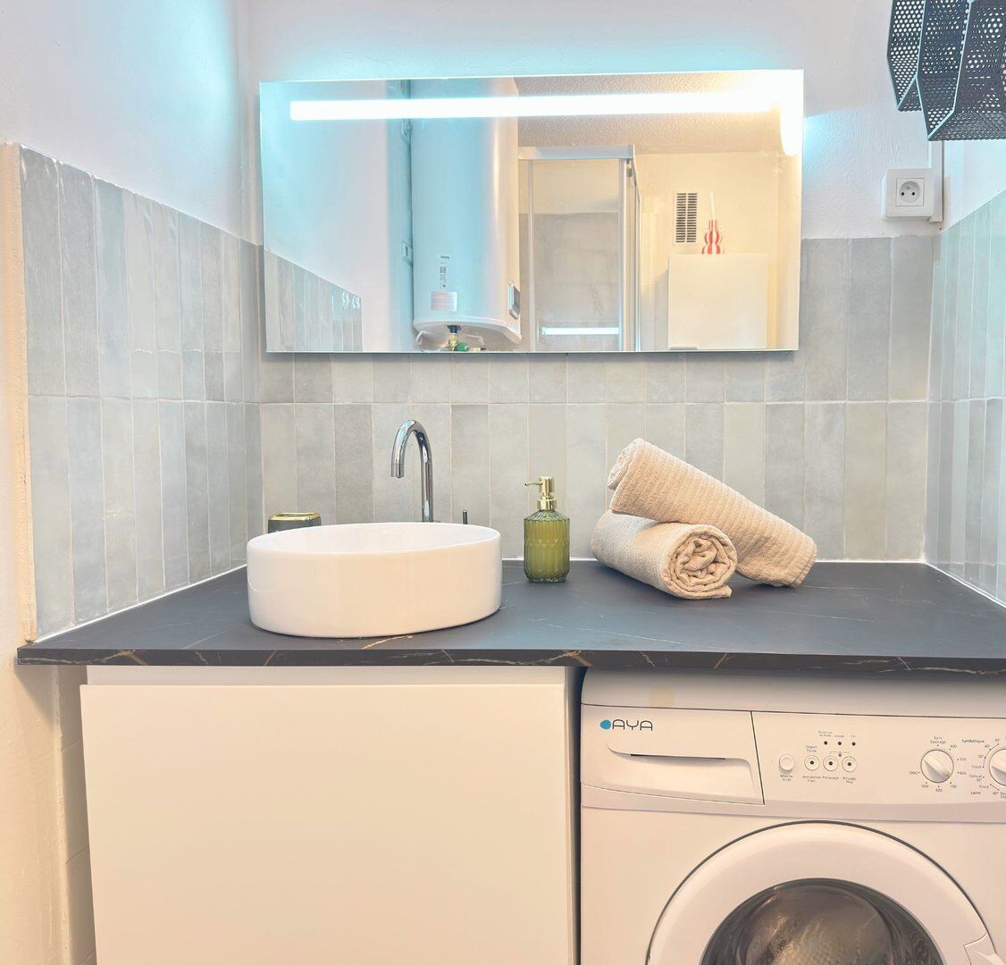 A modern bathroom with a round sink, a mirror, a towel, a soap dispenser, and a washing machine.