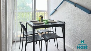 A balcony with a table set for two, chairs, and a view of greenery outside.