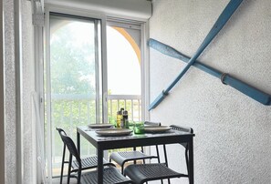 A balcony with a table set for two, chairs, and a view of greenery outside. - Le Studio de Lou, confort, beach & port (Carnon-Plage)