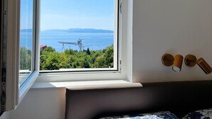 A room with a large window offering a view of a coastal landscape, including wind turbines and a body of water. - Sea View Apartment Rijeka-free Parking-6 People (Rijeka)