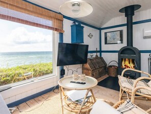 Habitació acollidora amb vista al mar, una llar de foc, mobles de vimet i una televisió.