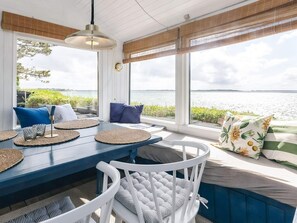 A sunlit room with a view of the water, featuring a blue table, white chairs, and a bench with cushions. - 4 Person Holiday Home in Martofte (Martofte)