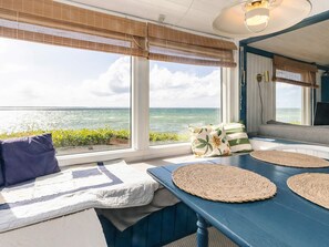 A room with a view of the ocean, a blue table with woven placemats, and a bench with cushions. - 4 Person Holiday Home in Martofte (Martofte)