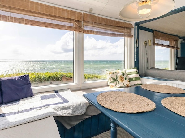 Una habitación con vista al océano, una mesa azul con individuales tejidos y un banco con cojines.