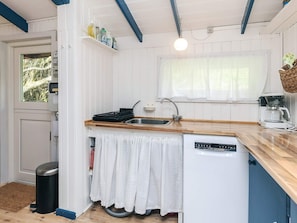 Una cocina compacta con un lavamanos, lavavajillas y una ventana con cortinas.