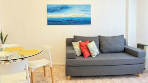 Een woonkamer met een grijze bank, een glazen tafel met stoelen en een schilderij aan de muur.