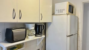 A kitchenette with a toaster, a coffee maker, and a microwave on a white cabinet.