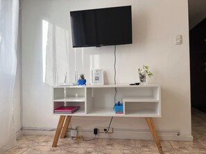 Ein weißes TV-Möbelstück mit einem flachbildfernseher darüber, ein weißes Regal mit einem roten Buch und eine kleine Pflanze rechts.