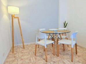 Ein Essbereich mit einem runden Glastisch, weißen Stühlen, Holzboden und einer Stehlampe.