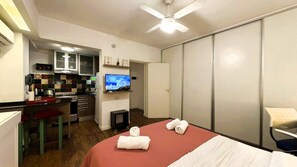 A compact hotel room with a bed, a small kitchenette, a television, and a sliding door closet.